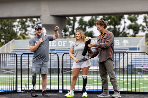 Adaptive athlete with a prosthetic leg stands with event speakers during a Challenged Athletes Foundation gathering focused on access to sport and adaptive equipment.