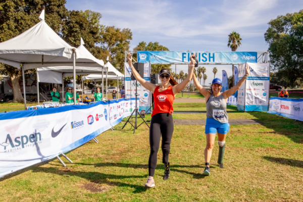 Two participants cross the finish line with raised arms at the Challenged Athletes Foundation San Diego Triathlon Challenge, celebrating an adaptive sports achievement.
