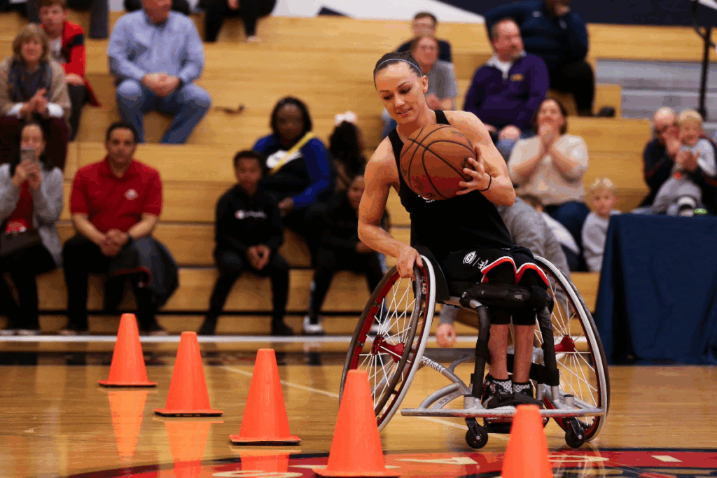 Team USA athlete, Megan Blunk, in a wheelchair navigating basketball cones during a skills drill, with spectators watching