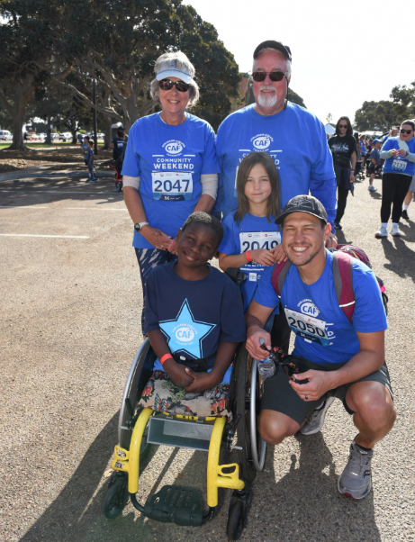 A family group, including a young participant in a wheelchair, poses together before the start of the 5K Walk + Roll.