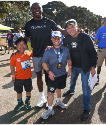 A group of friends and families smile and pose for a photo before starting the 5K Walk + Roll event.
