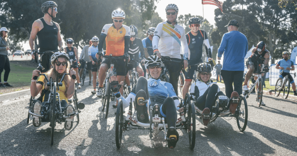 Athletes on handcycles smile at the starting line surrounded by cyclists at the San Diego Triathlon Challenge.