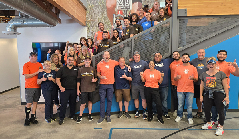 Group of volunteers in orange shirt stand next to and on a set of stairs in the CAF headquarters as they pose for a photo together.