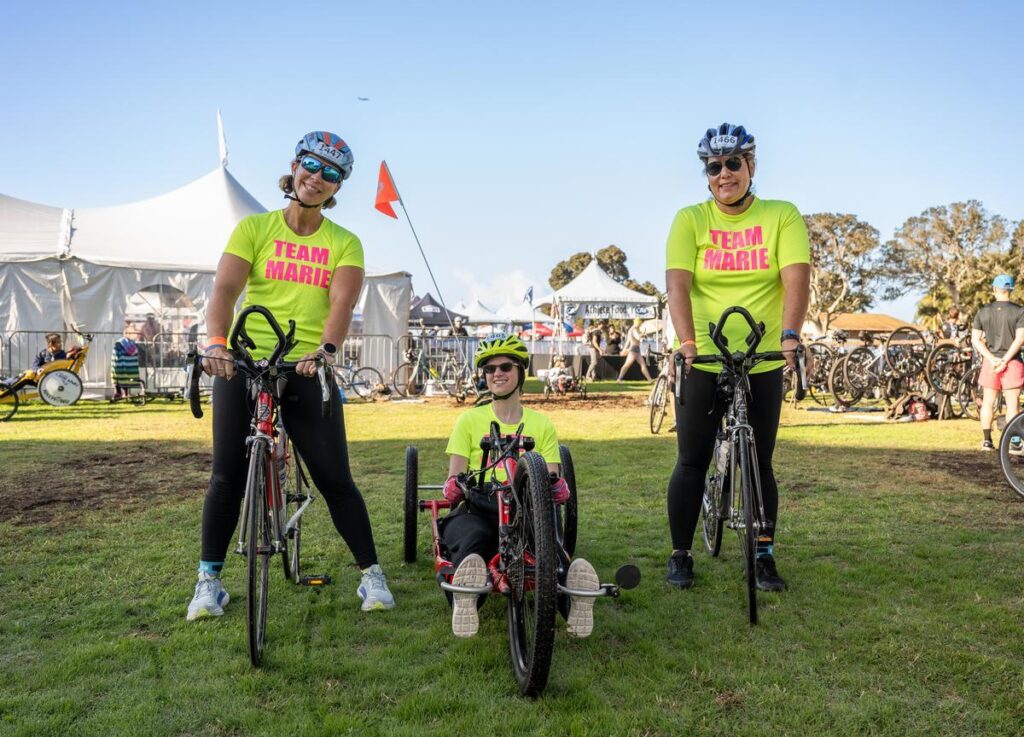 Two upright cyclists and a handcyclists in yellow t-shirts with the wording "Team Marie" at the San Diego Triathlon Challenge