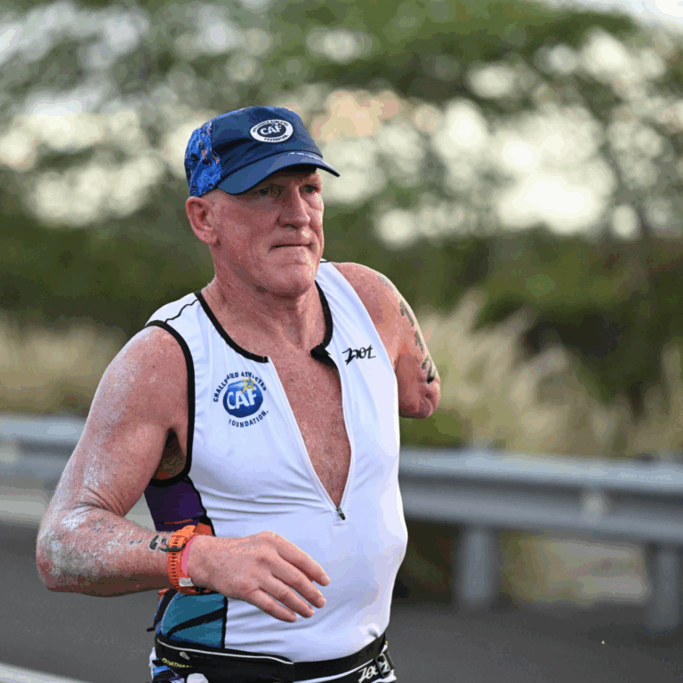 Close-up of Willie Stewart running on a road during a triathlon, wearing a CAF tri-suit and cap.
