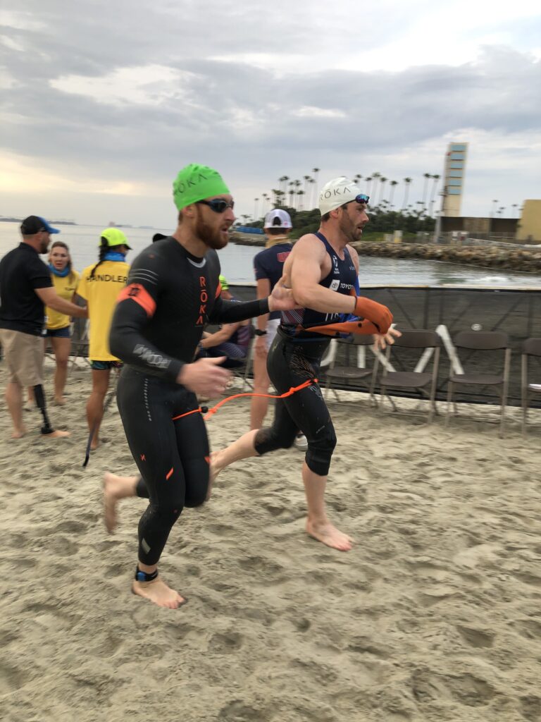 Brad Snyder tethered to guide Greg Billington as they run out of the water during the swim portion of a triathlon.