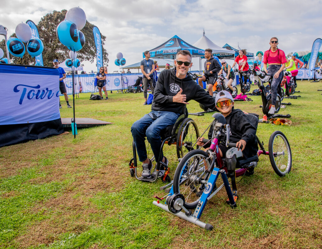 Glenn Hartrick smiling with a young athlete in a handcycle at CAF’s Tour de Cove event