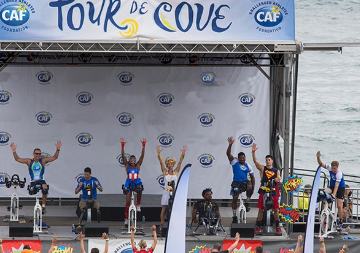 Instructors and athletes on stationary bikes leading a Tour de Cove cycling session on stage overlooking the ocean