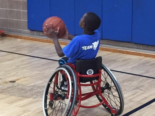 Athlete in a red wheelchair prepares to shoot a basketball inside a gymnasium
