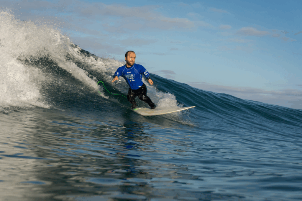 Athlete with dwarfism (Ryan Gambrell) surfs a large wave with control and balance during an adaptive surf competition