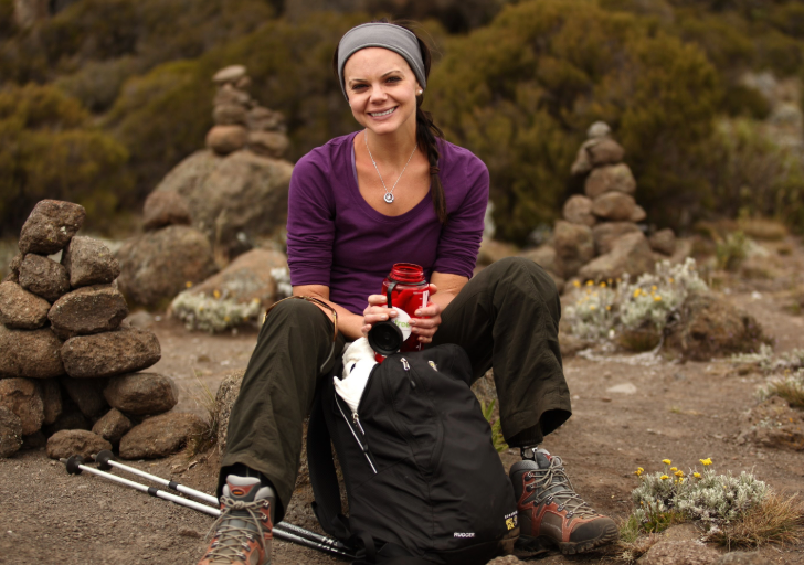 Tara Butcher sits on a trail surrounded by rocks, smiling and holding a water bottle during a hike.