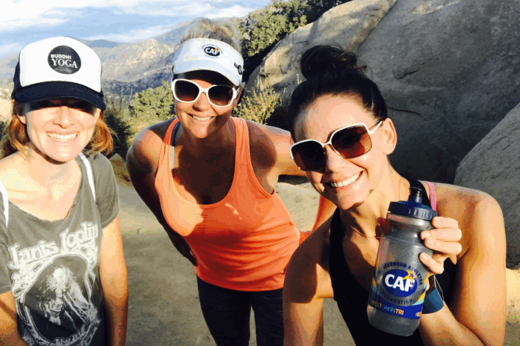 Tara Butcher and two friends smile during a hike, wearing sunglasses and holding a CAF water bottle.