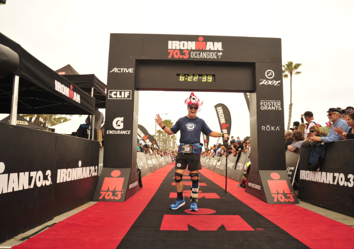 An athlete crosses the Ironman 70.3 finish line on a red carpet, amidst cheering spectators.