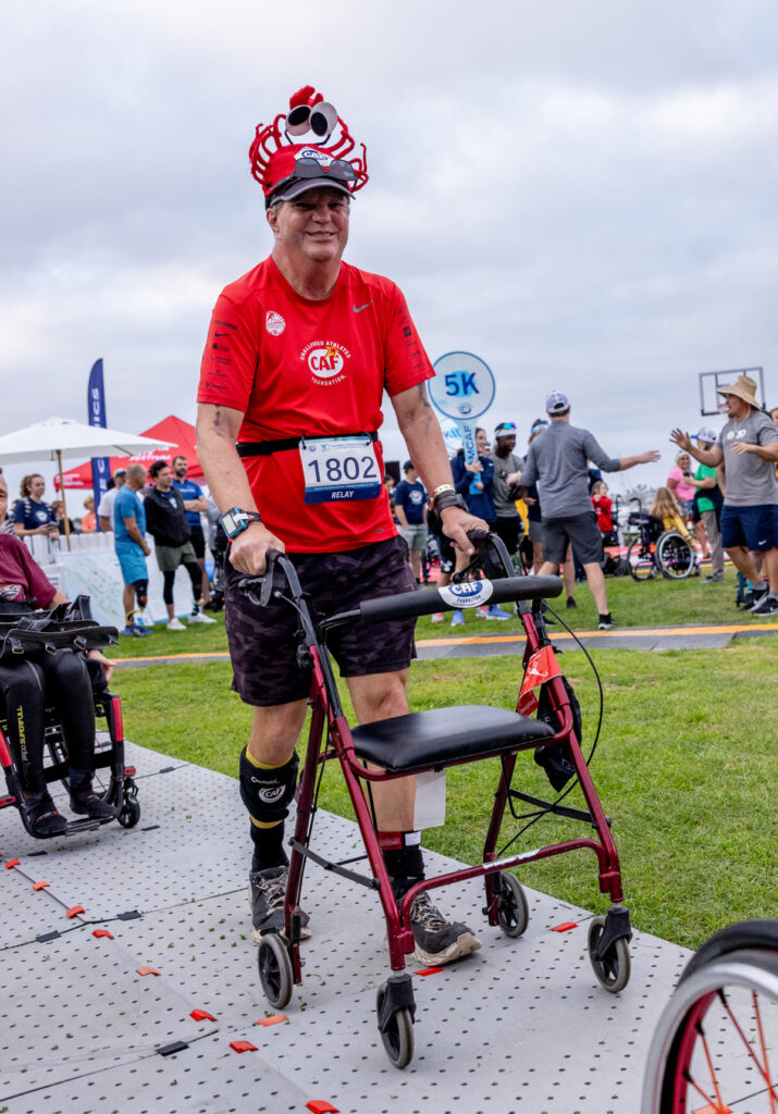 A relay participant walking with a red walker, wearing a red T-shirt and a novelty crab headpiece.