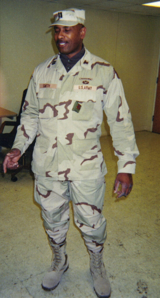 Person in a tan camo military uniform standing indoors.