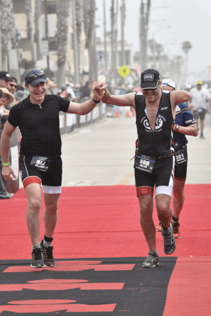 Miles O’Brien raises his teammate’s hand in triumph as they cross the Ironman 70.3 Oceanside finish line together.