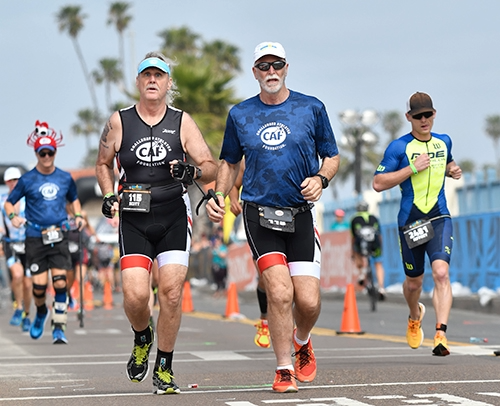 A group of athletes, including a blind runner and guide, participate in a road race, surrounded by other competitors.