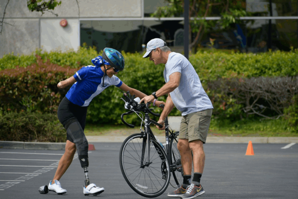 Coach assists an athlete with a prosthetic leg as they mount a road bike during paratriathlon training.