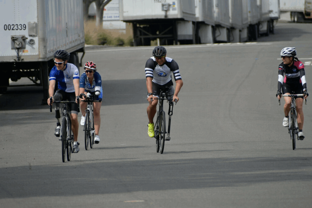 Four cyclists, including athletes with prosthetic legs, ride together on the road during a paratriathlon session.