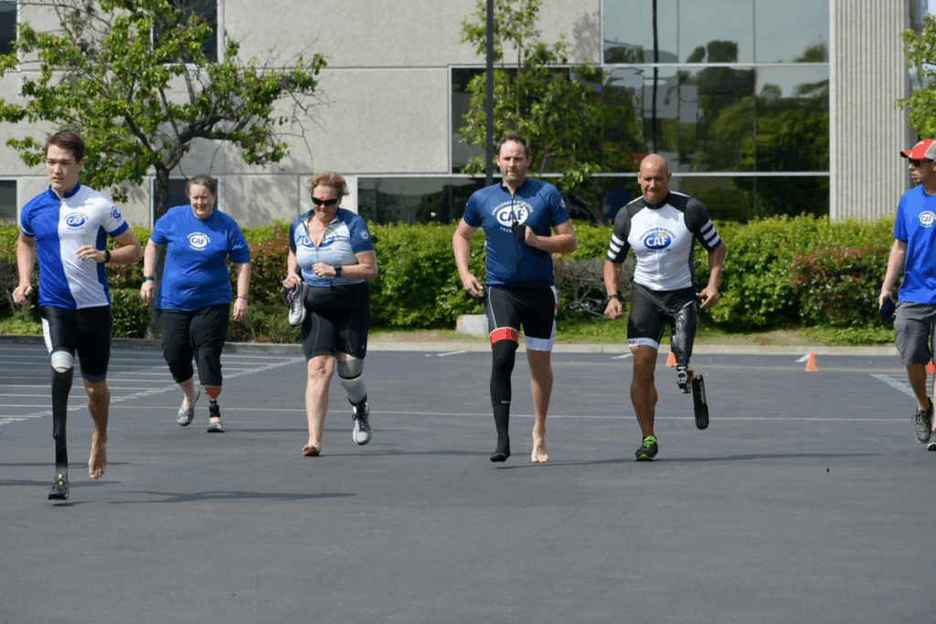 Group of paratriathletes with prosthetic legs and supporters running together in a parking lot during training.