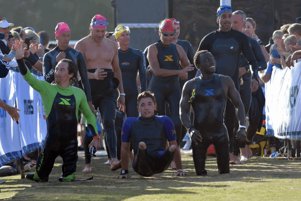 Paratriathletes including Rudy Tolson Garcia and Roderick Sewell exit the water and head toward transition, smiling and high-fiving spectators after completing the swim portion of a triathlon.