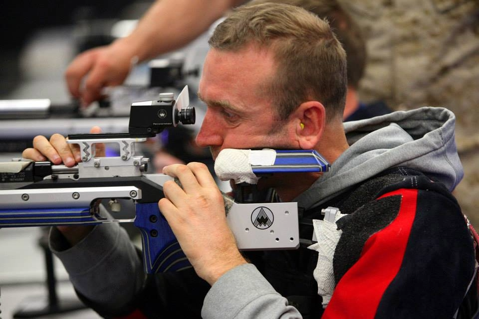 Athlete aiming carefully through the sight of a competition air rifle at an indoor range.