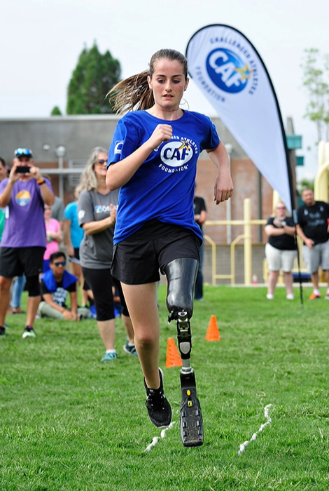 Young athlete with a running blade runs toward the camera on a grassy field, focused on the finish line during a CAF clinic.