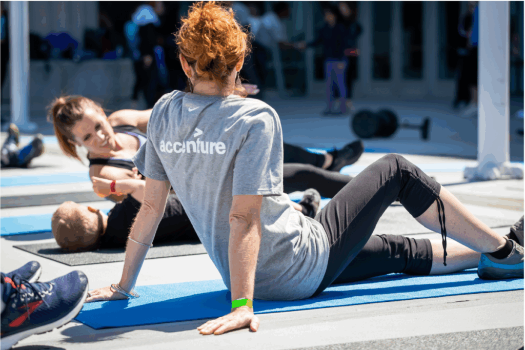 Participants stretch on exercise mats during a Move to Include workout, including one person wearing an Accenture T-shirt in the foreground.