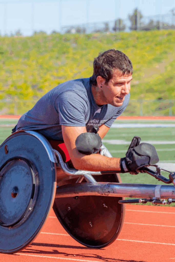 A wheelchair racer powers down the track in a racing chair, wearing gloves and focused on the push stroke.