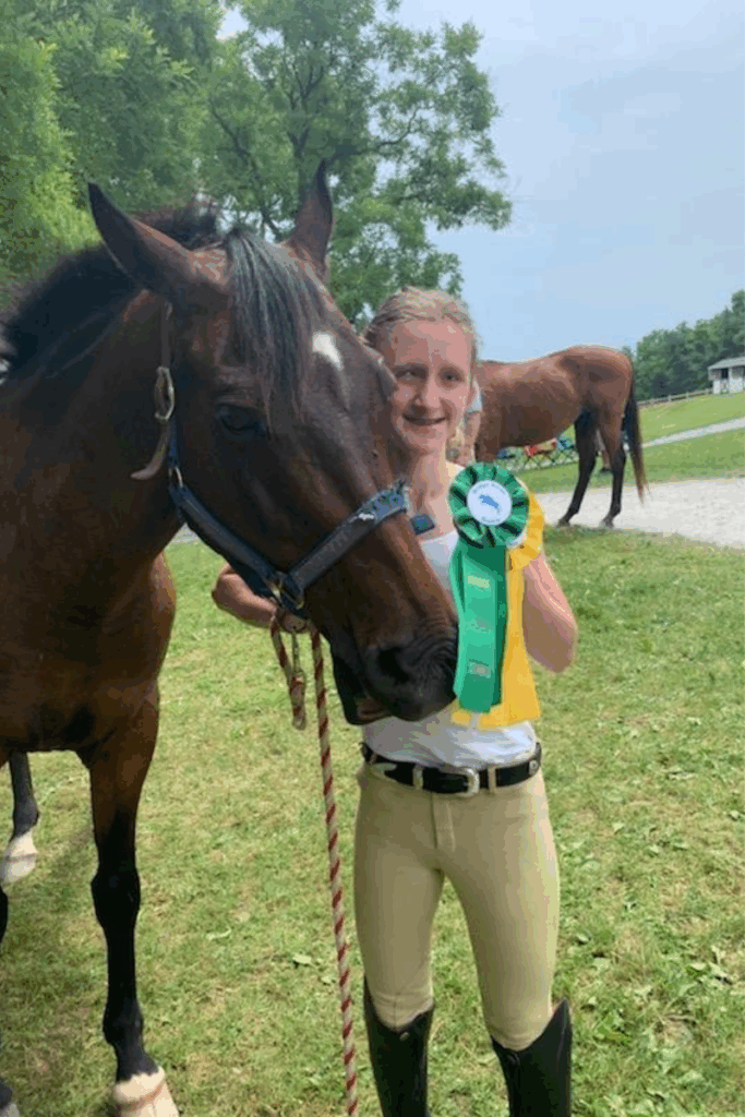 A rider holds a green and yellow ribbon next to a horse at a competition.