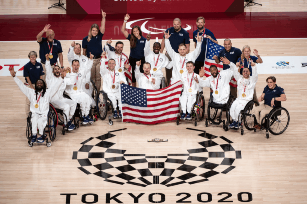 Team USA wheelchair basketball athletes and staff celebrate with gold medals and an American flag on the Tokyo 2020 court.