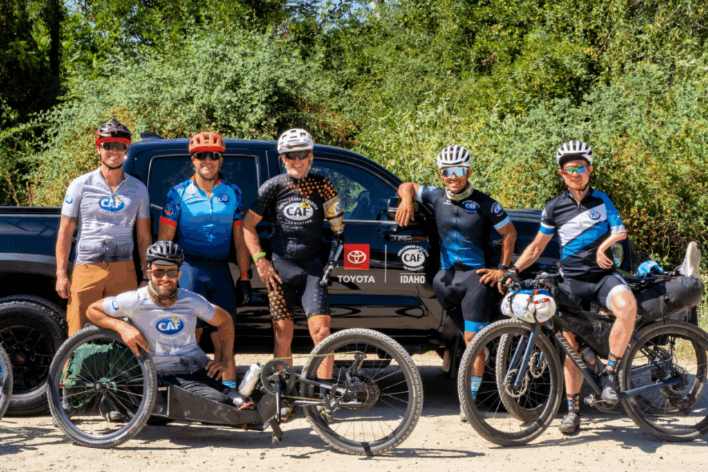 Six adaptive cyclists pose with their bikes in front of a Toyota CAF-Idaho support vehicle during a ride.