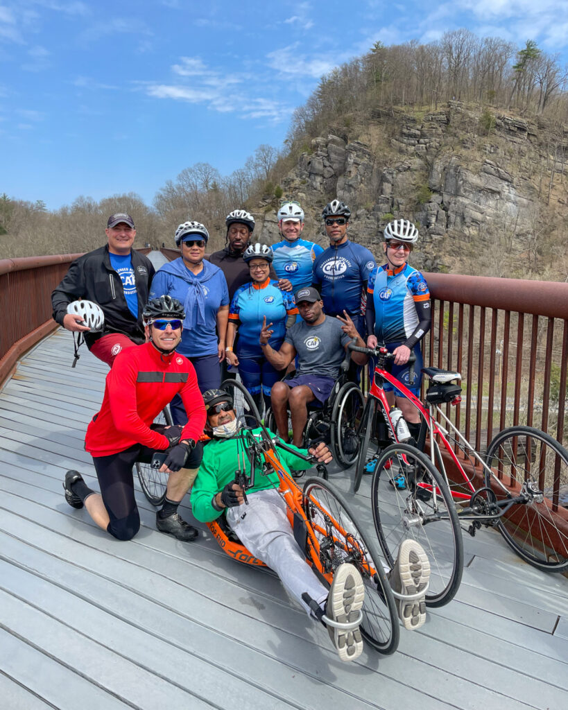 A group of people on a bridge with rocky cliffs and a blue sky in the background.