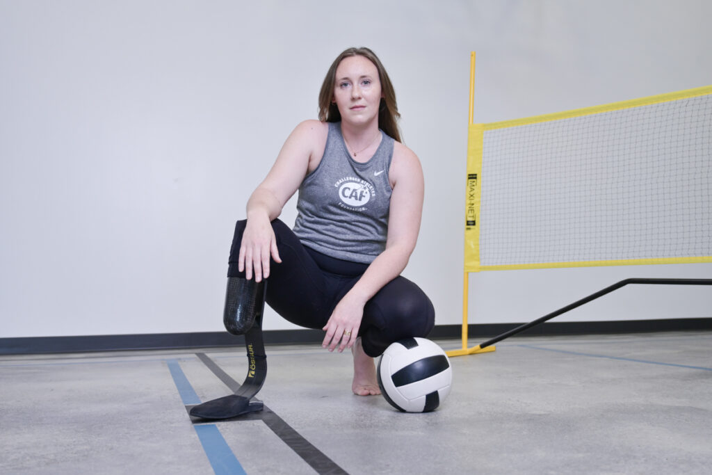 Person kneeling with a prosthetic leg, hand on a volleyball, next to a yellow net.