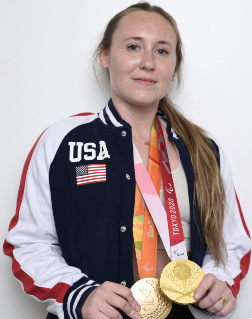 Person in a USA jacket holding gold medals from Rio 2016 and Tokyo 2020.