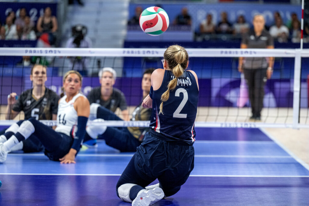 A sitting volleyball player, number 2, prepares to receive a ball mid-air on a blue court.