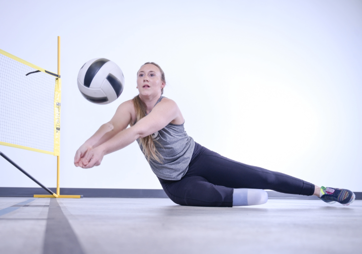 Woman with a prosthetic leg playing seated volleyball on an indoor court.