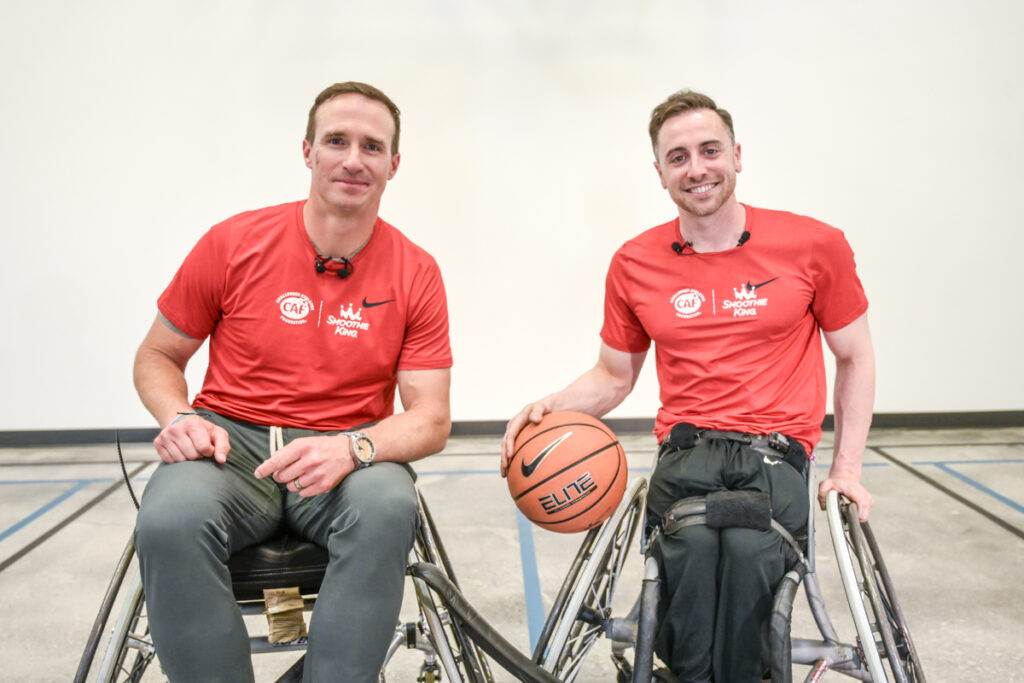 Two people in wheelchairs wearing red T-shirts, one holding a basketball.