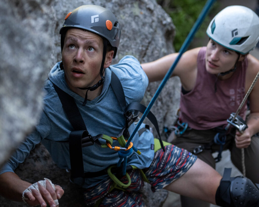 Two climbers in helmets and gear focused while scaling a rocky surface.