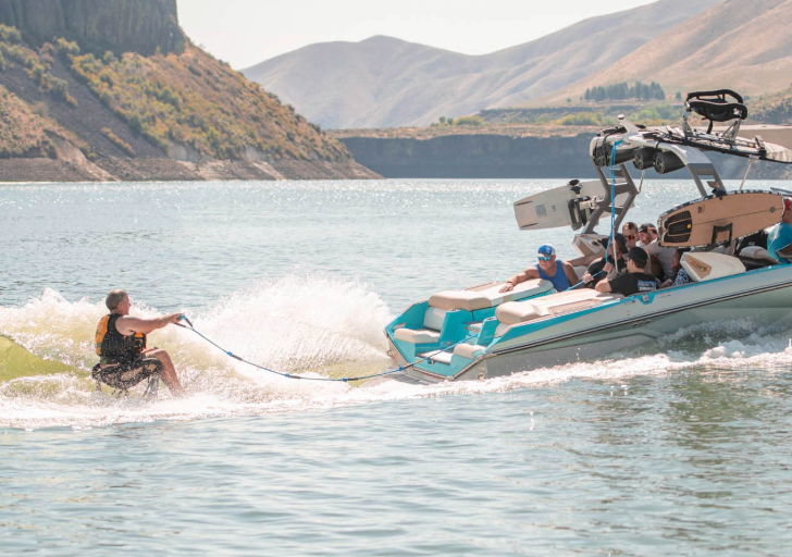 Powerboat towing a wakeboarder on a lake surrounded by hills.