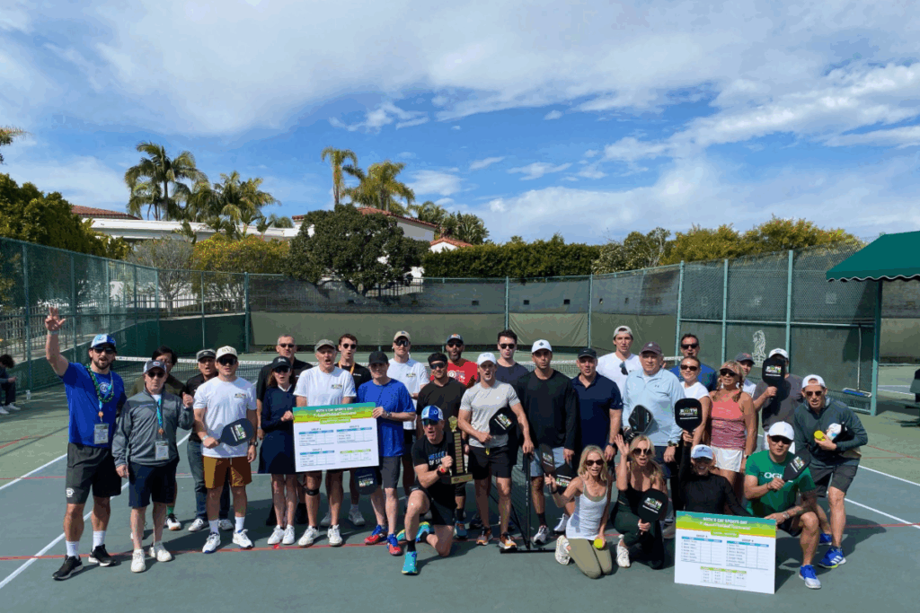 A large group of participants pose on a tennis court, holding pickleball paddles and signs during a CAF sports day event.