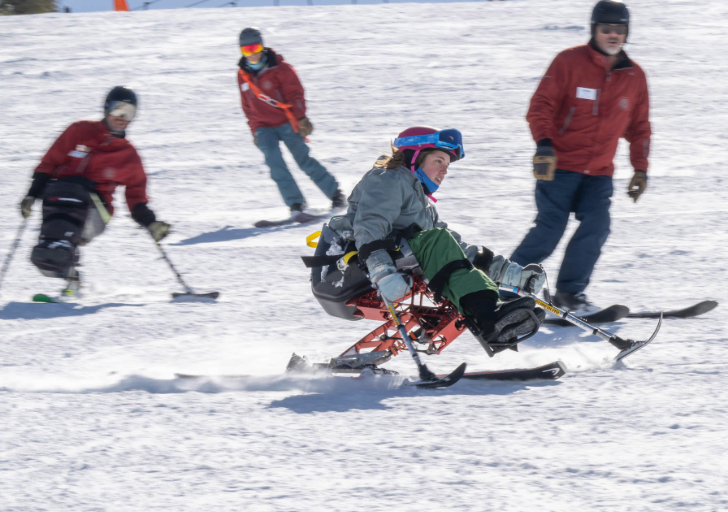 Person using a sit-ski on a snowy slope with others in the background.
