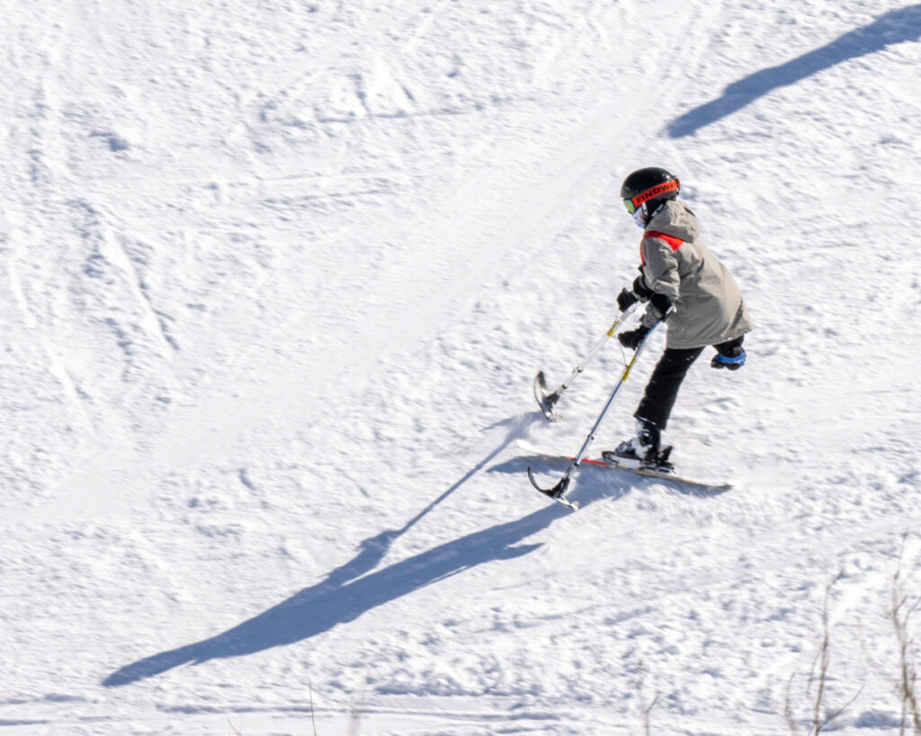 A skier in a grey jacket skis down a snowy slope.
