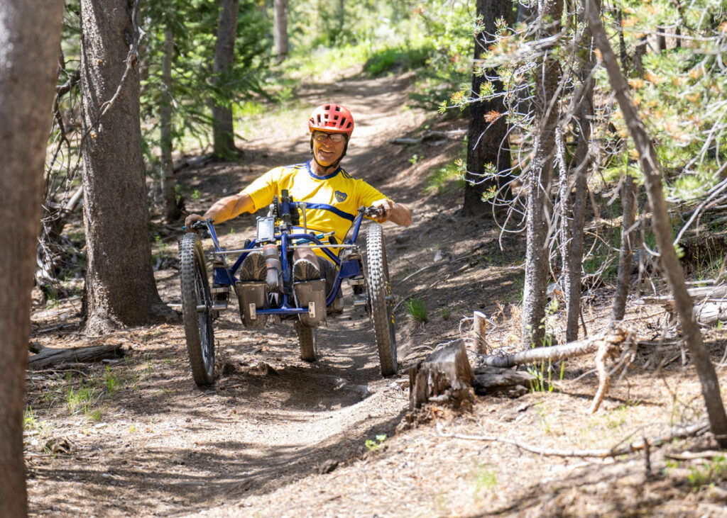 A person riding an adaptive mountain bike in a wooded mountain setting.