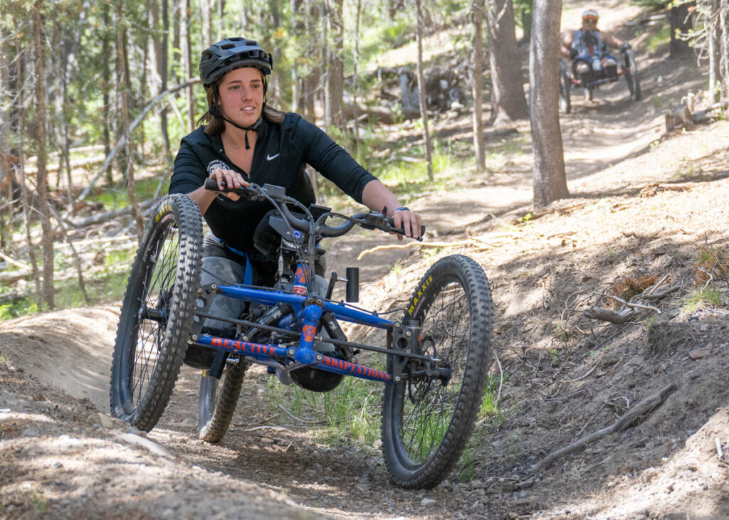 A person riding an adaptive mountain bike in a wooded mountain setting.