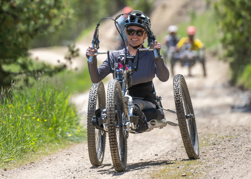 A person riding an adaptive mountain bike in a wooded mountain setting.