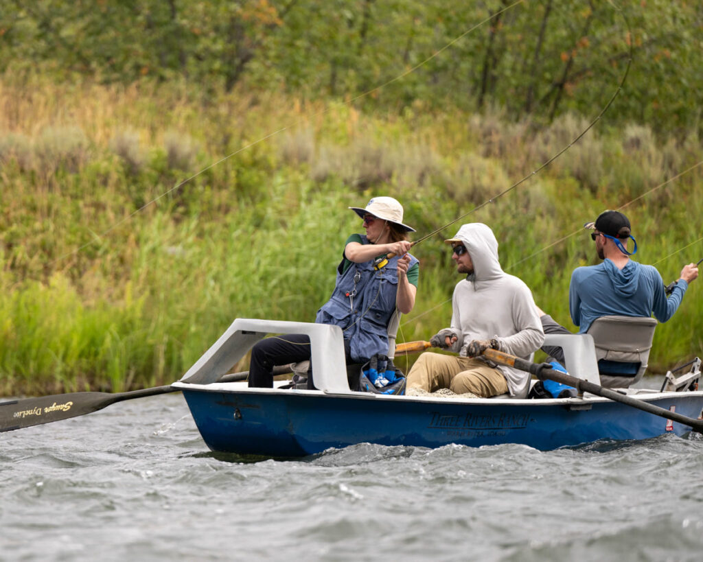 Three people fly fishing from a boat in choppy waters. 