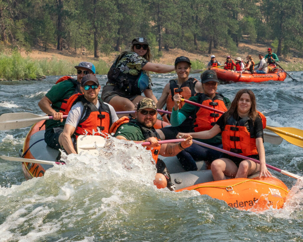 Group of people rafting on a river with life jackets and paddles.