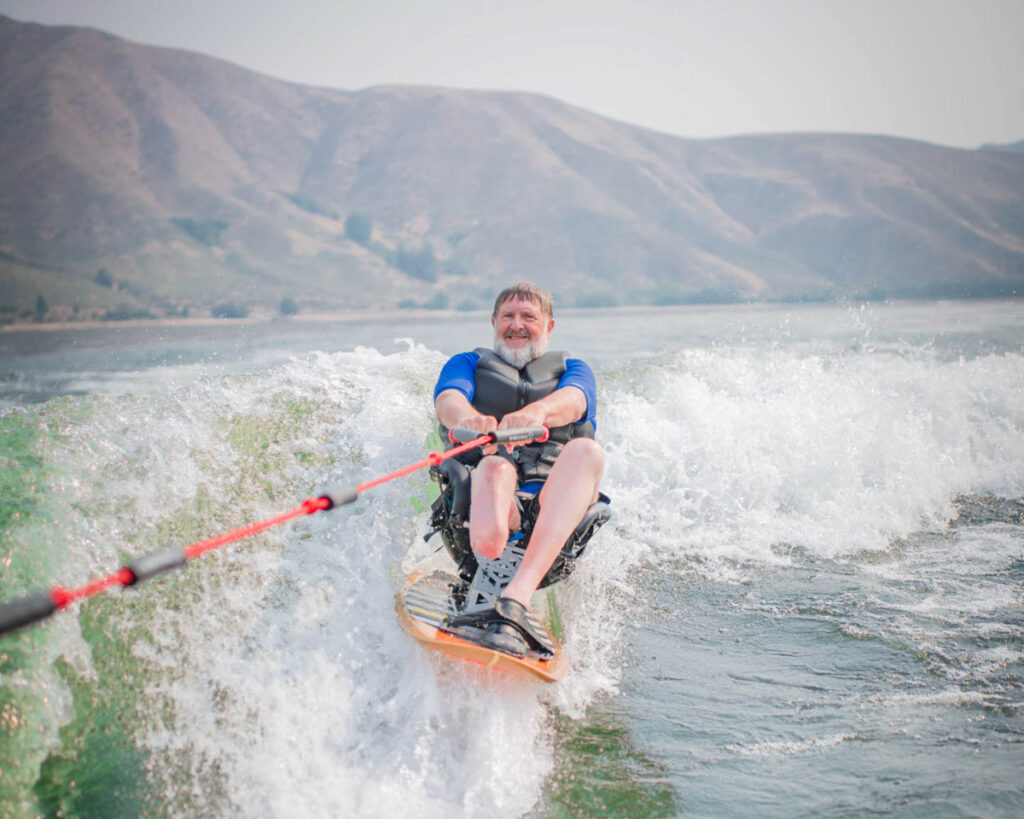Person wakeboarding on a lake, holding a red and black rope, with hills in the background.