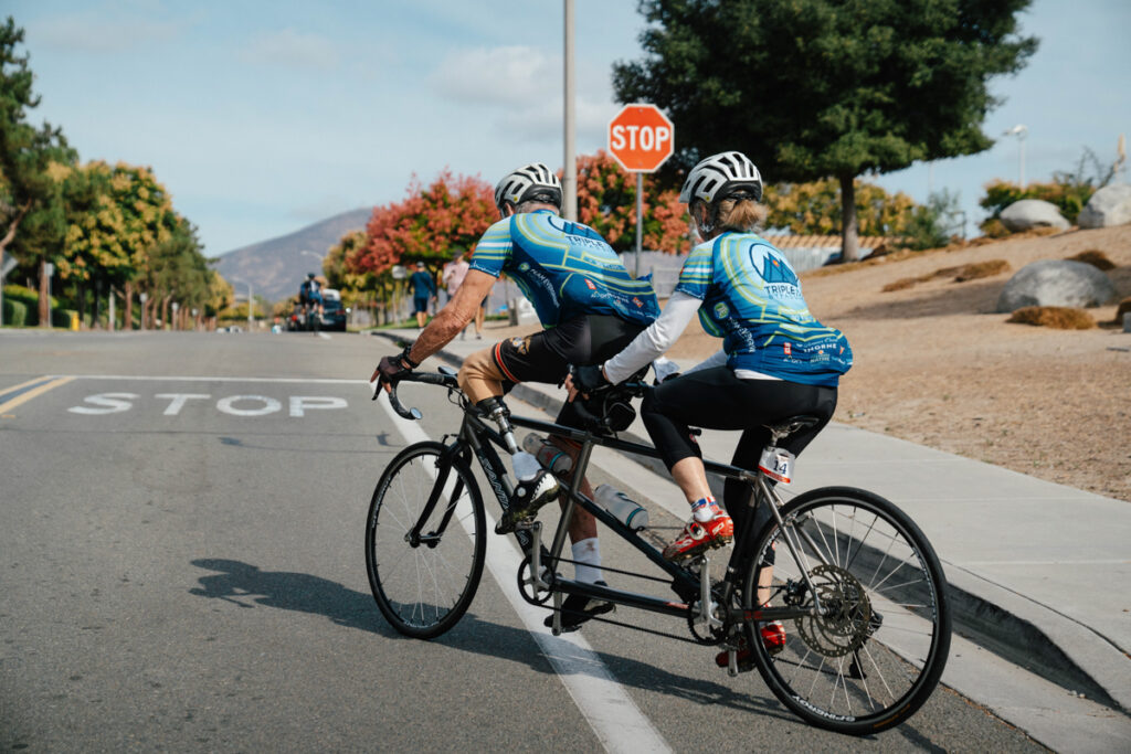 Two cyclists on a tandem bike approaching a stop sign on a suburban street.